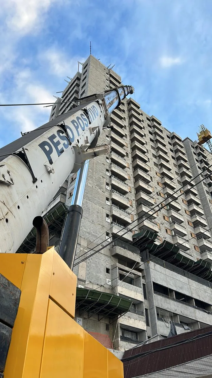 Vista em contrapicado da lança do guindaste Peso Positivo sobre o edifício em construção com seção do mastro da grua visível