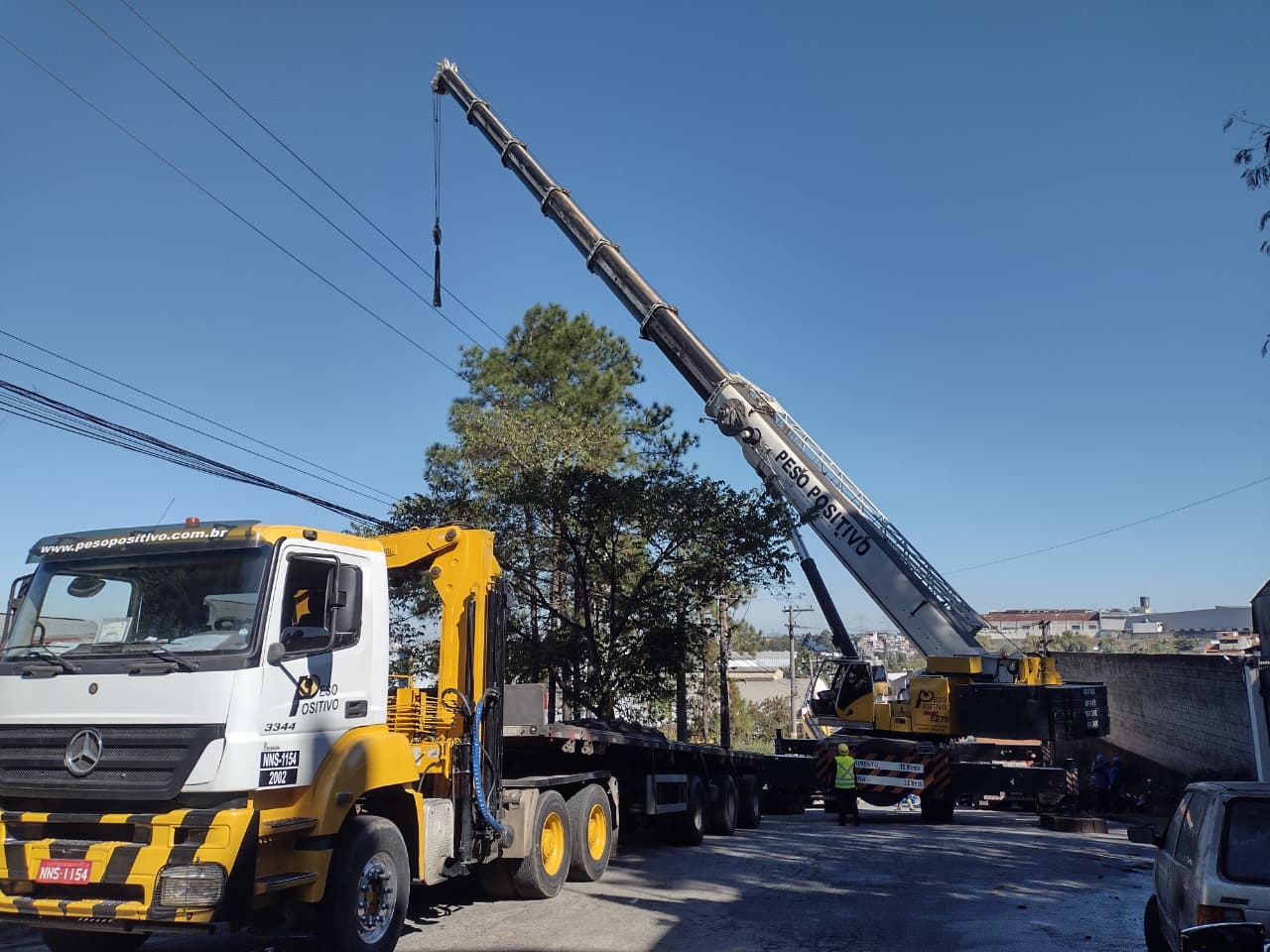 Guindaste Peso Positivo com patolas estendidas e caminhão Mercedes amarelo com prancha de transporte