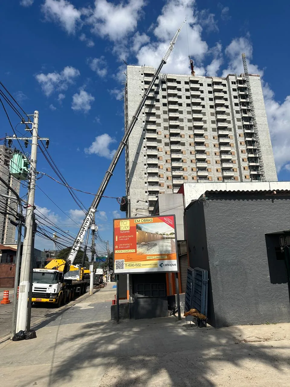 Guindaste Grove do Peso Positivo com jib treliçado e caminhão Scania com munck posicionados em via urbana ao lado do edifício em construção