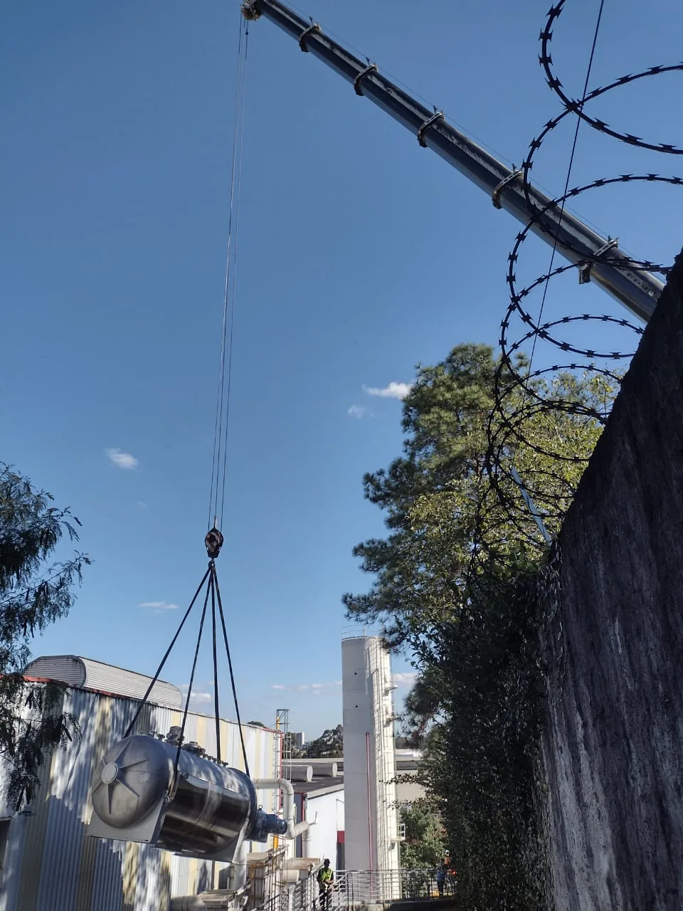 Autoclave cilíndrica de aço inoxidável içada por guindaste sobre muro industrial na Sika em Osasco