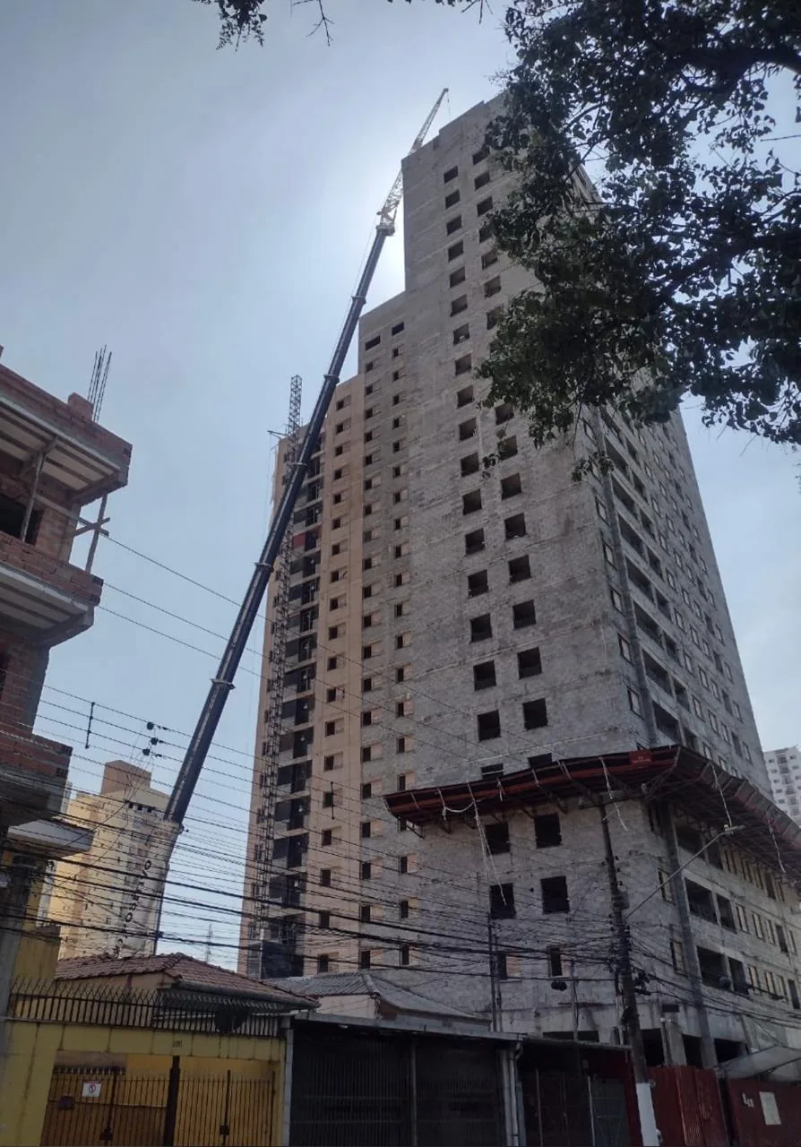 Guindaste móvel de grande porte com lança telescópica e jib treliçado estendidos até edifício de aproximadamente 20 andares em construção